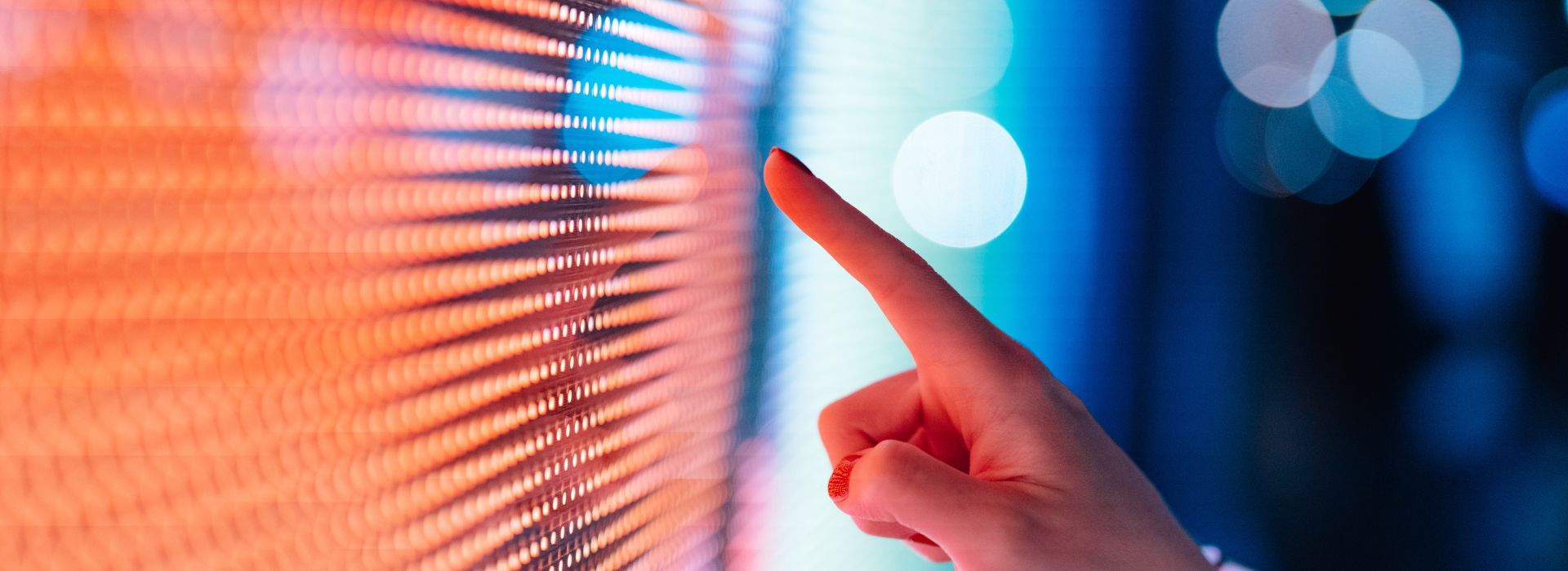 Hand pointing at a colourful LED screen with orange and blue pixels.